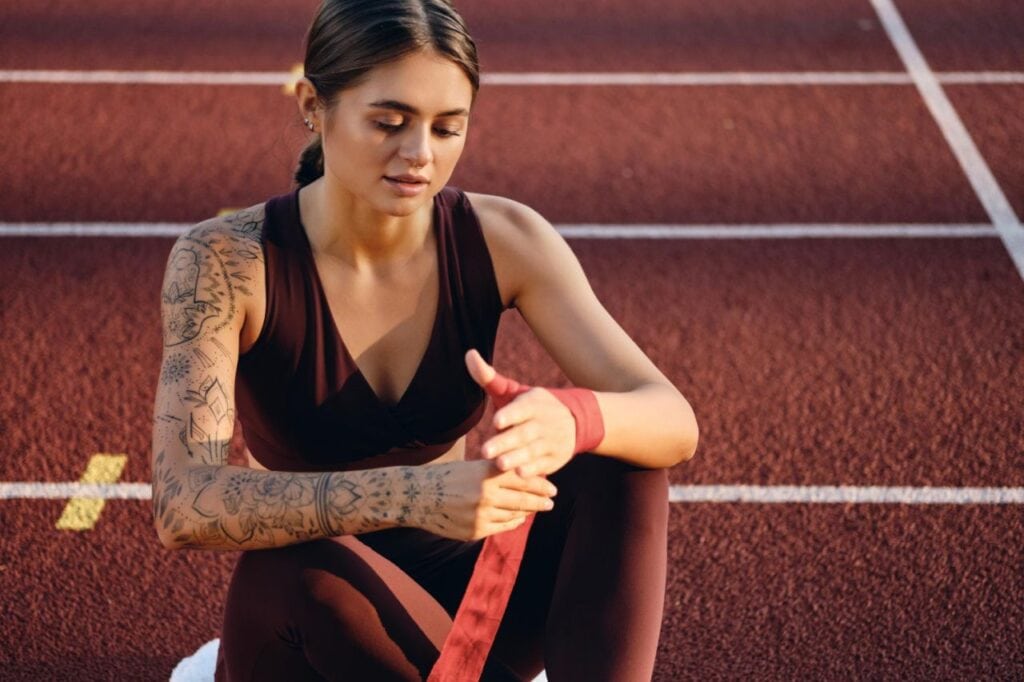 beautiful sporty girl with tattooed hand sportswear dreamily wrapping red boxing bandage hand stadium
