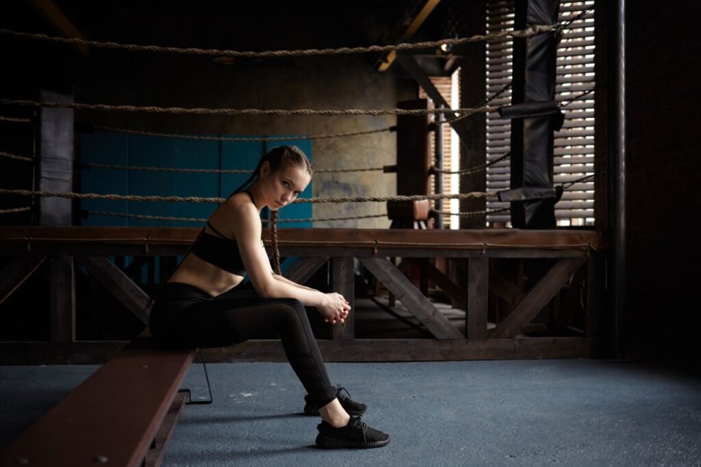 tired young female with slim fit body sitting bench after boxing workout modern gym wearing black sports outfit sneakers